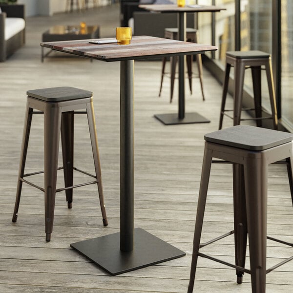 A Lancaster Table & Seating bar height table with textured mixed plank finish and a square base plate with stools on an outdoor patio.