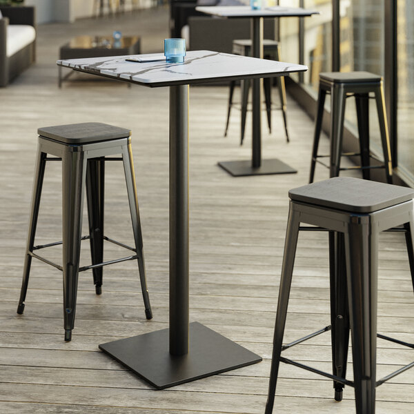 A Lancaster Table & Seating bar height table with a square base plate and stools on a patio.