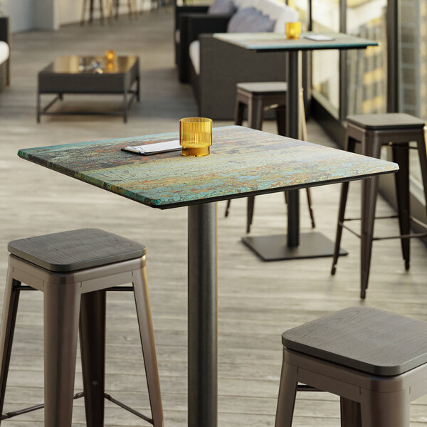 A Lancaster Table & Seating square table top with a textured metal finish and a candle on it.