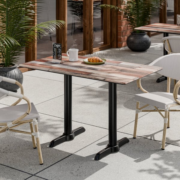 A rectangular outdoor table with a mixed wood plank-style top and black metal legs, surrounded by white cushioned chairs on a patio.