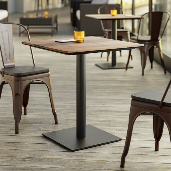 A Lancaster Table & Seating Excalibur square table with a textured farmhouse finish on a wood floor with two brown chairs