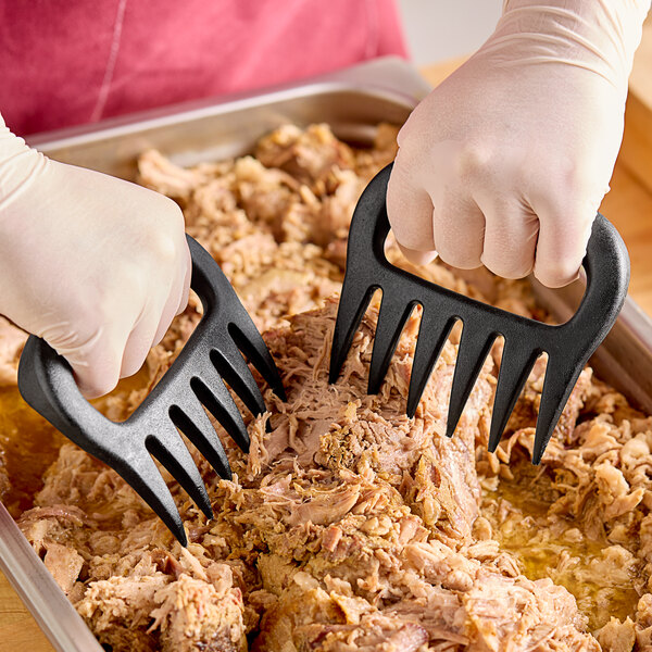 A person using black nylon meat shredding claws to shred meat in a tray.