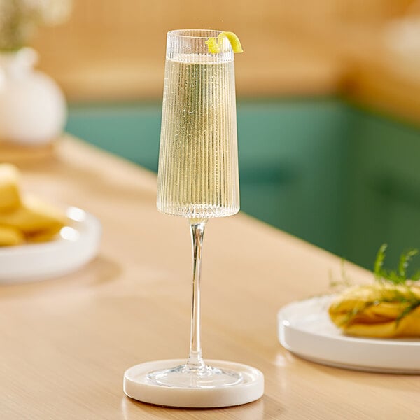 An Acopa Lore flute glass of champagne sits on a table.