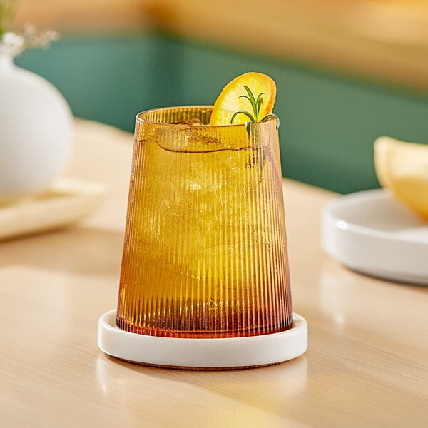 An Acopa Lore amber stemless wine glass with a drink and a slice of orange on a table.