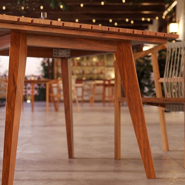 A wooden Lancaster Table & Seating Virelli outdoor table with chairs in the background.