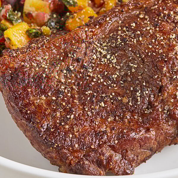 A piece of meat with Badia Table Grind Black Pepper and vegetables on a plate.