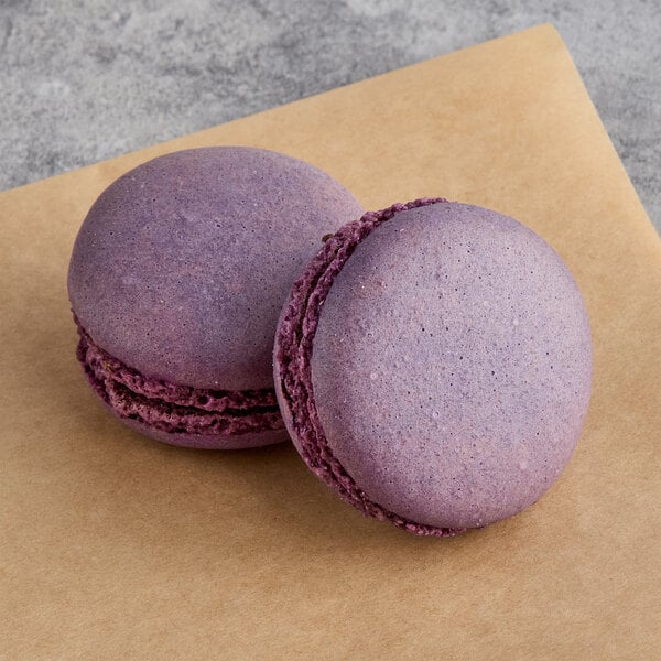 Two White Toque French Lemon Lavender macarons with purple filling on a brown surface.