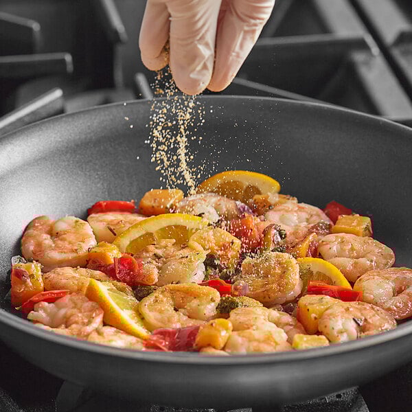 A person sprinkling Badia Sazon Tropical Seasoning on shrimp in a pan.