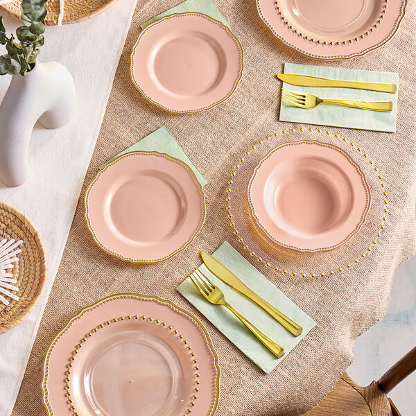 A table setting with pink Visions plastic bowls with gold vintage rims and gold utensils.