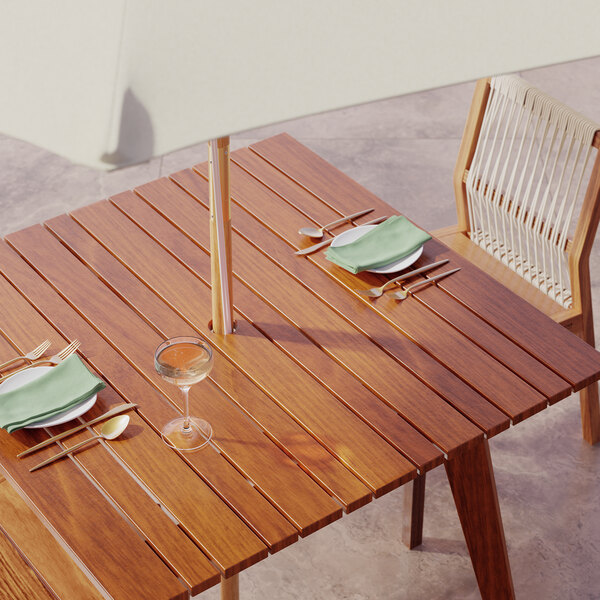 A Lancaster Table & Seating outdoor table with a white umbrella, plates, and silverware on a patio.