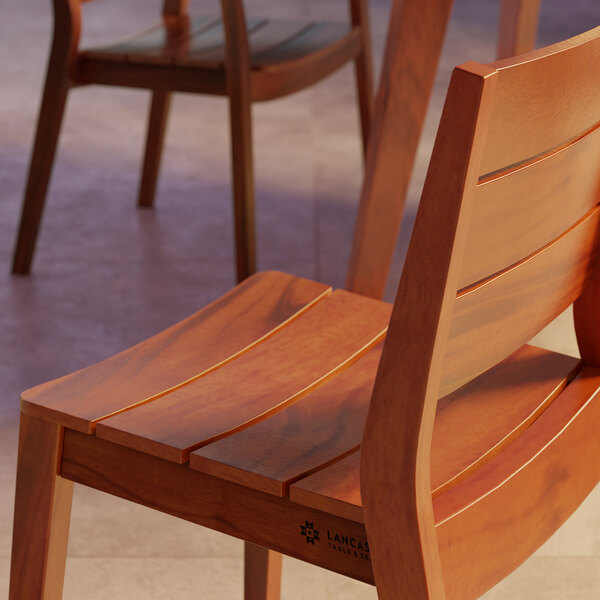 A Lancaster Table & Seating Virelli Tigerwood slat back outdoor side chair on a table in a restaurant dining area.