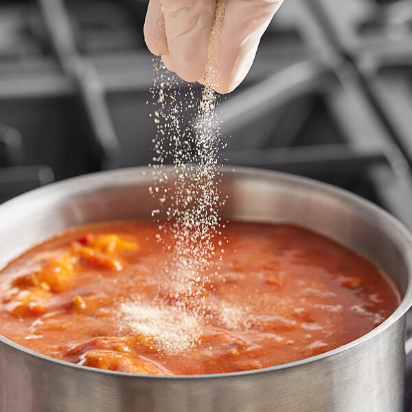 A person's hand sprinkling Badia granulated onion into a pot of food.