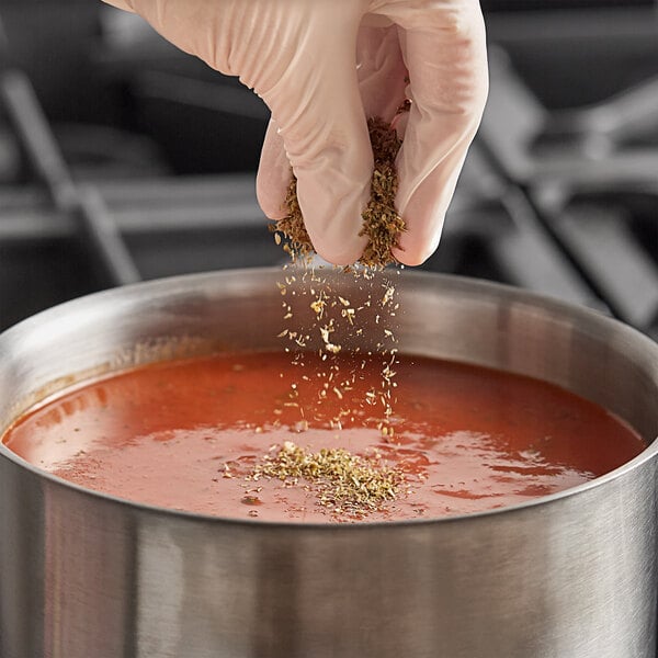 A person sprinkling Badia Whole Oregano into a pot of soup.