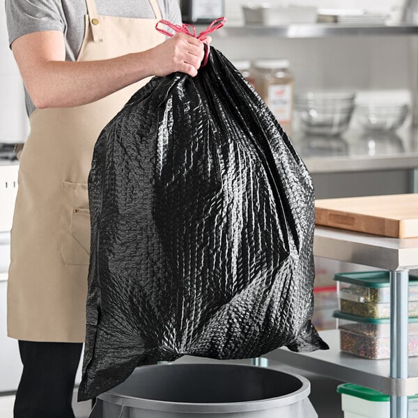A man holding a Lavex black drawstring trash bag in a kitchen.