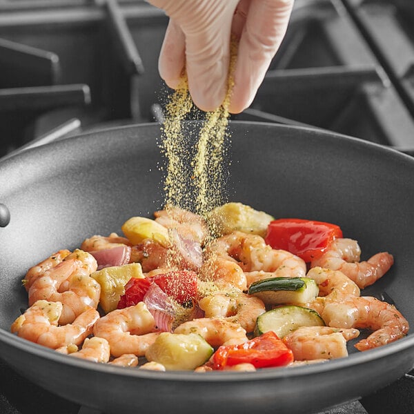 A person sprinkling Badia Lemon Pepper on a pan of food.