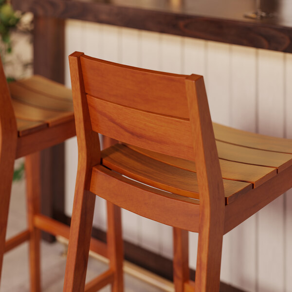 Two Lancaster Table & Seating Virelli Tigerwood slat back outdoor barstools next to a counter.