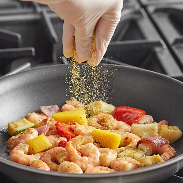 A person sprinkling Badia Mango Pepper seasoning on a pan of shrimp.