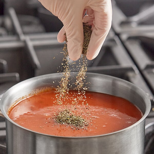 A hand pouring Badia Basil Leaves into a pot of soup.