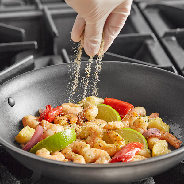 A person seasoning food in a pan with Badia Lime Pepper.