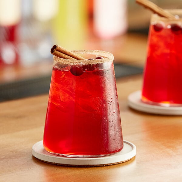 A glass of Paradise Cranberry Juice with a cinnamon stick on a table.