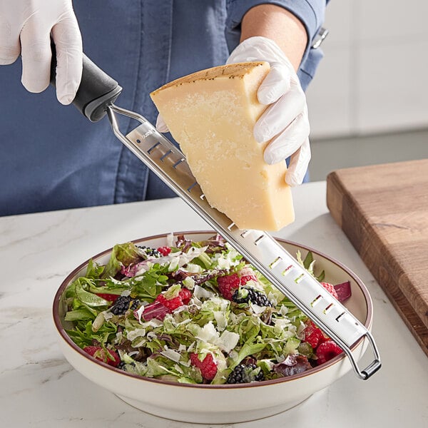 A handheld grater shaver being used to grate cheese over a bowl of salad.