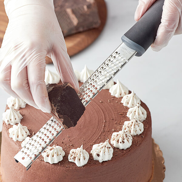 A person's hand using a Choice stainless steel handheld grater to grate chocolate.