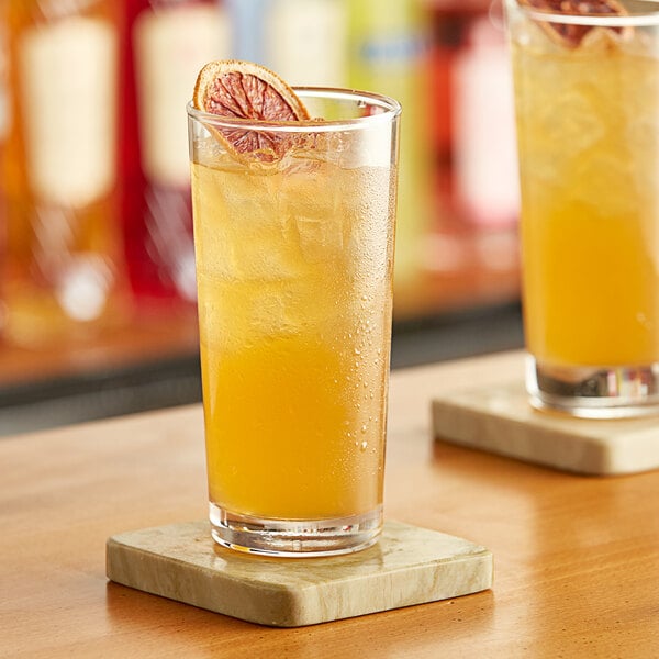 A glass of Paradise Energy Drink with ice and a slice of orange on a coaster.