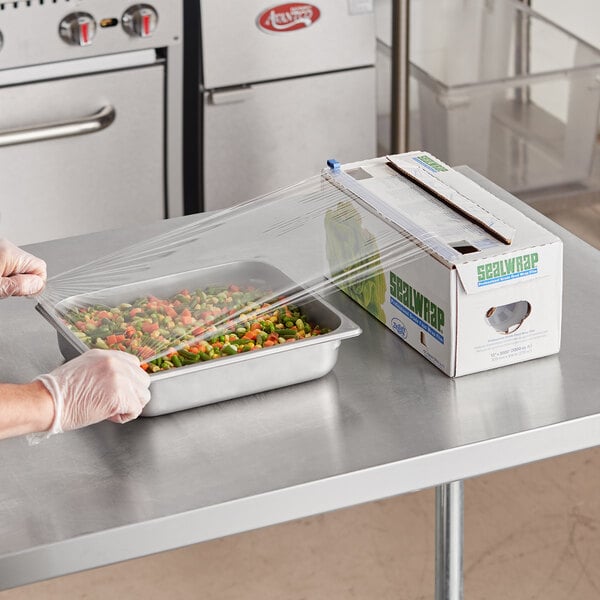 A person using Berry Heavy-Duty Plastic Film to wrap a tray of vegetables.