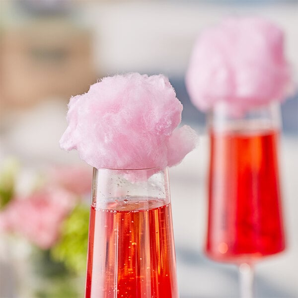 A pink cotton candy on top of a glass filled with pink liquid.