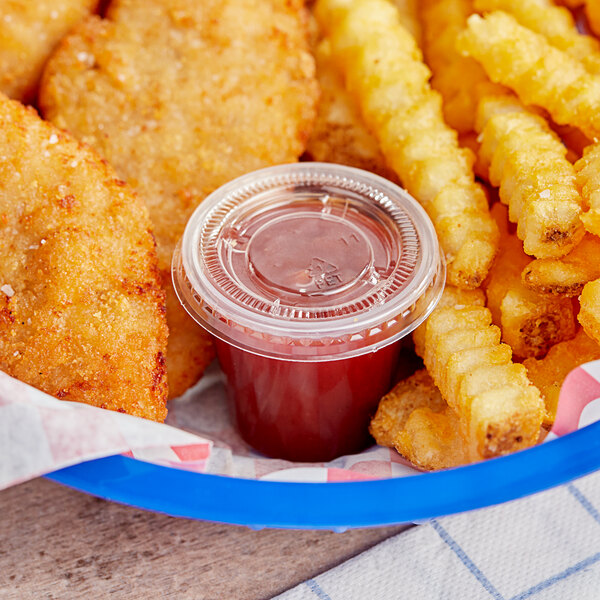 A bowl of chicken nuggets and french fries with a clear plastic container of red liquid.