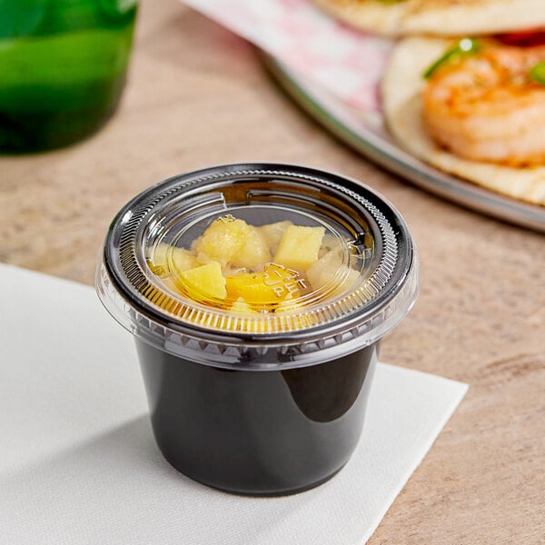 A black plastic Choice souffle cup with a PET plastic lid containing food.