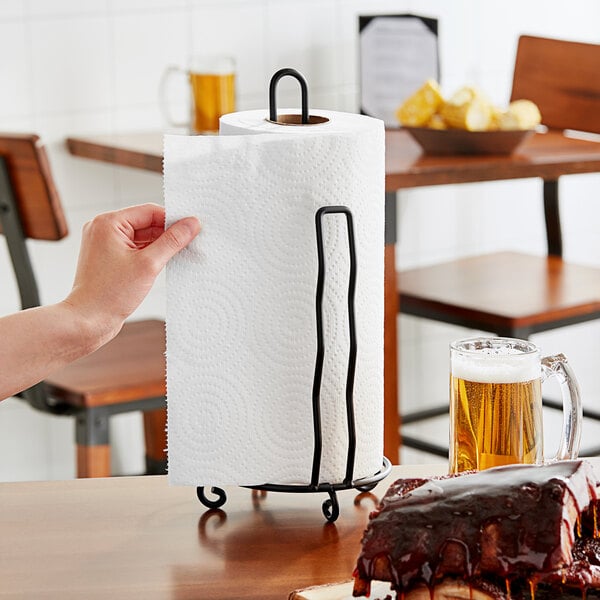 A hand holding a Lavex paper towel roll over a plate of food on a table.