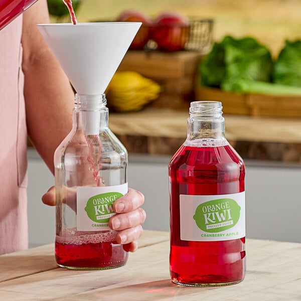 A woman pours red liquid into a clear glass juice bottle.