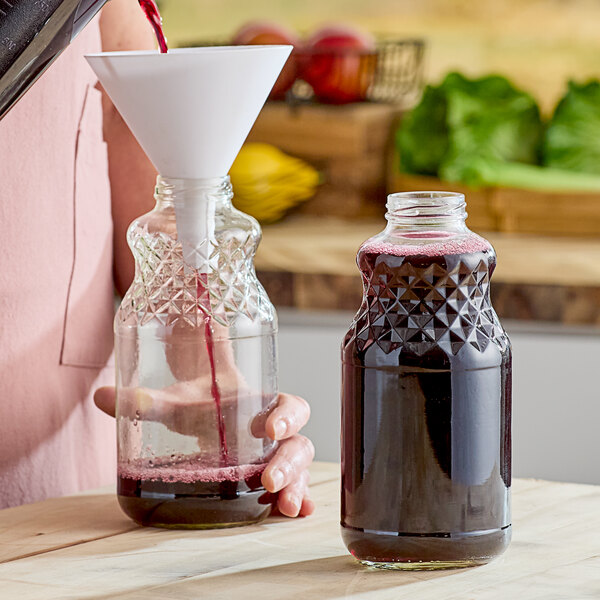 A woman pouring juice from a glass into a clear glass juice bottle.