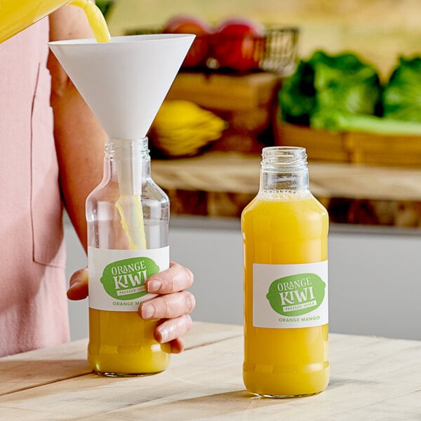 A person pouring orange juice into a clear glass juice bottle.