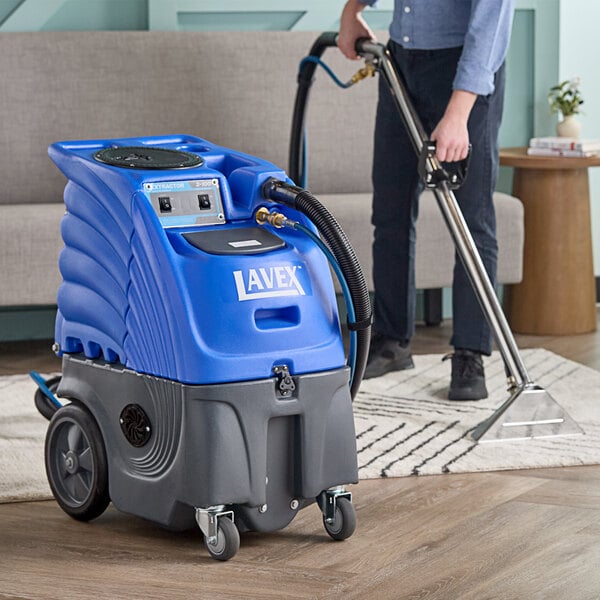 A man using a Lavex carpet extractor to clean a carpet with black hoses.