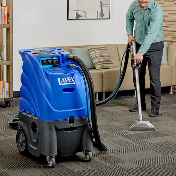 A man using a Lavex carpet extractor with hoses to vacuum a carpet.