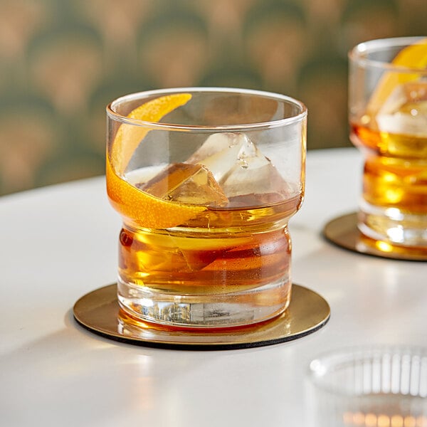 Two Libbey Newton rocks glasses with drinks and orange slices on a white table.