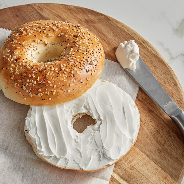 A bagel with WayFare vegan cream cheese on a wooden board with a knife.