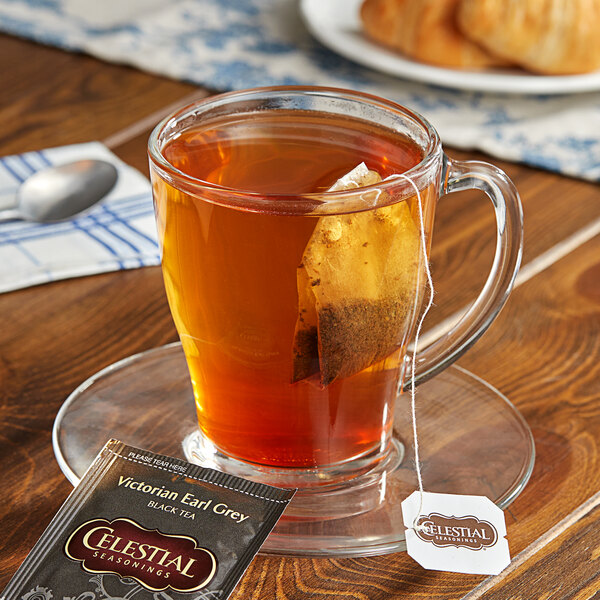 A glass cup of Celestial Seasonings Victorian Earl Grey tea with a tea bag in it on a saucer.