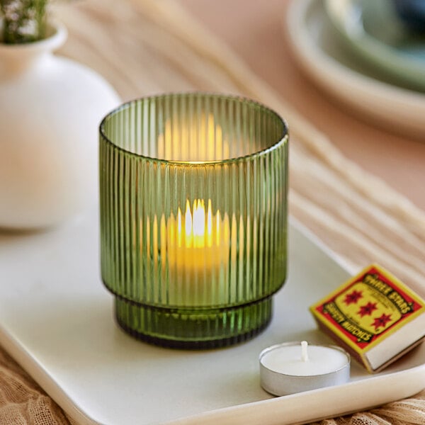 A green glass Acopa Lore tealight holder with a lit white candle inside.