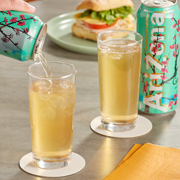 A person pouring AriZona Green Tea from a can into a glass of ice.