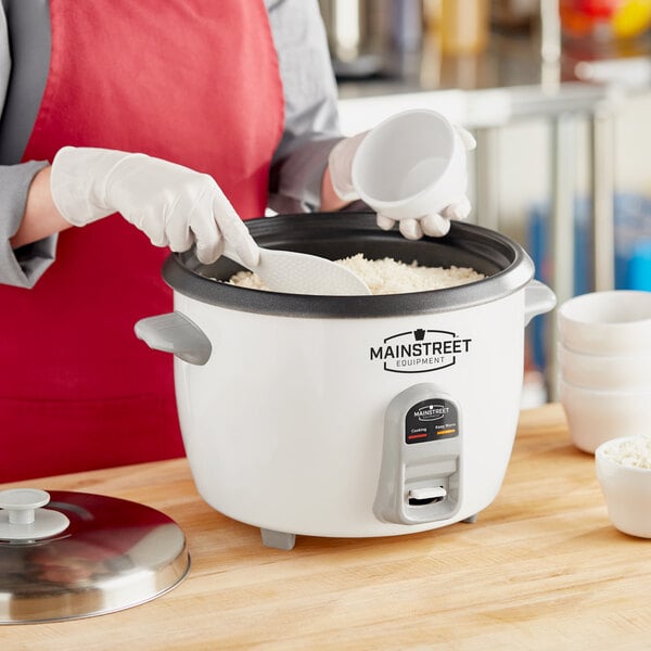 A woman in a red apron using a Main Street Equipment commercial rice cooker to cook rice.