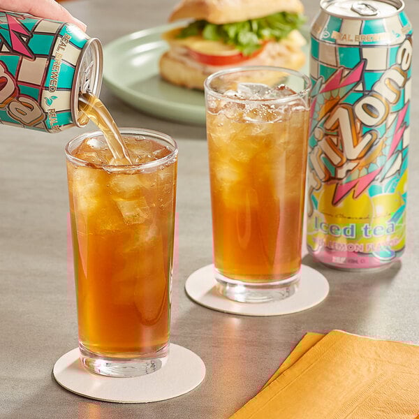 A hand pouring AriZona Lemon Iced Tea into a glass.