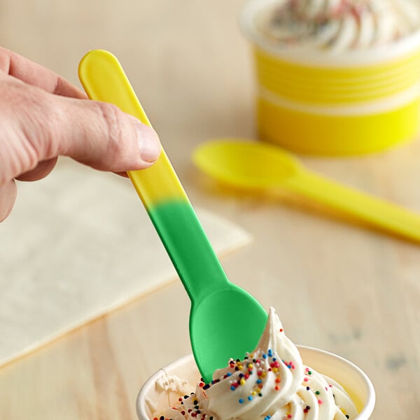 A hand holding a yellow and green color-changing spoon over a cup of ice cream.