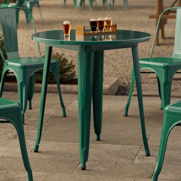 A Lancaster Table & Seating emerald green round outdoor table with chairs on a stone surface.