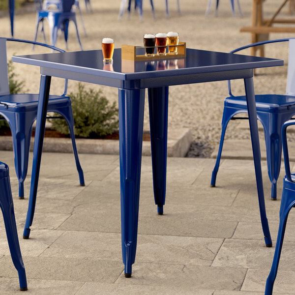 A square sapphire blue metal outdoor table with matching chairs, set on a stone patio.