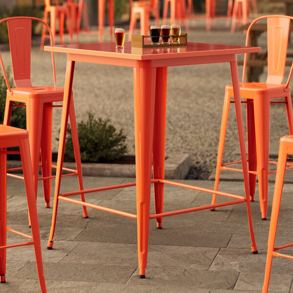 A Lancaster Table & Seating orange bar table set up on an outdoor patio.