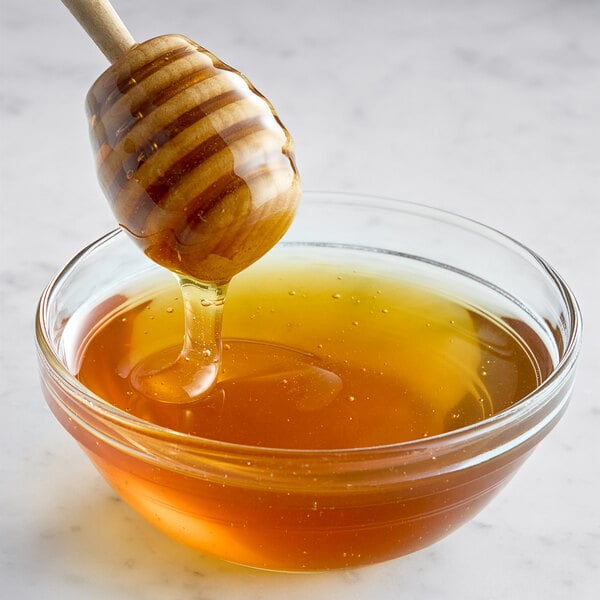 A honey dipper dripping honey into a bowl.