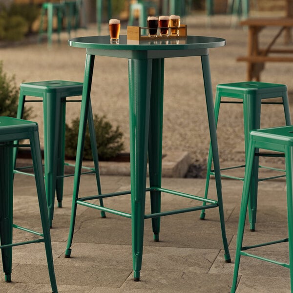 A Lancaster Table & Seating round emerald green table with green bar stools on a stone surface.